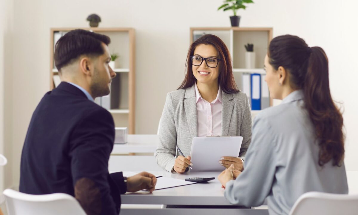 Female insurance broker holding a clipboard while discussing with a couple.