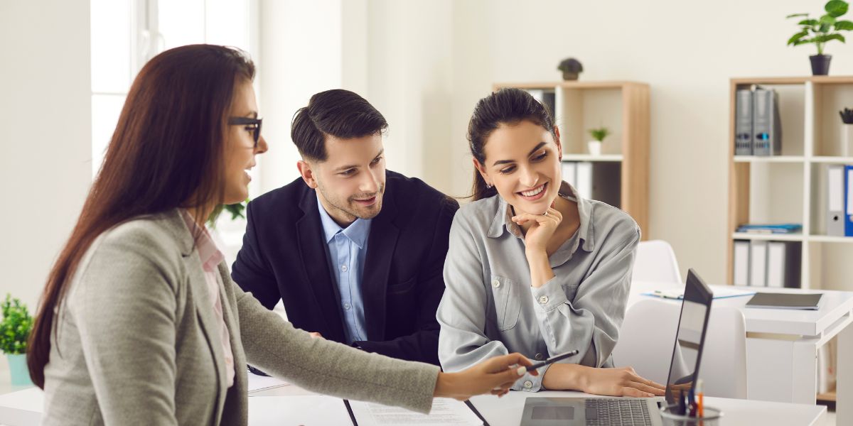 Female insurance broker explaining details to a smiling couple using a laptop.