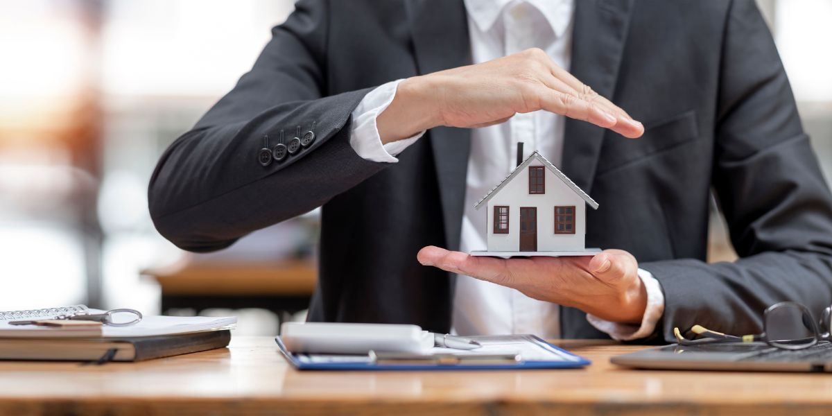 Businessperson holding a small house model with hands in a protective gesture.