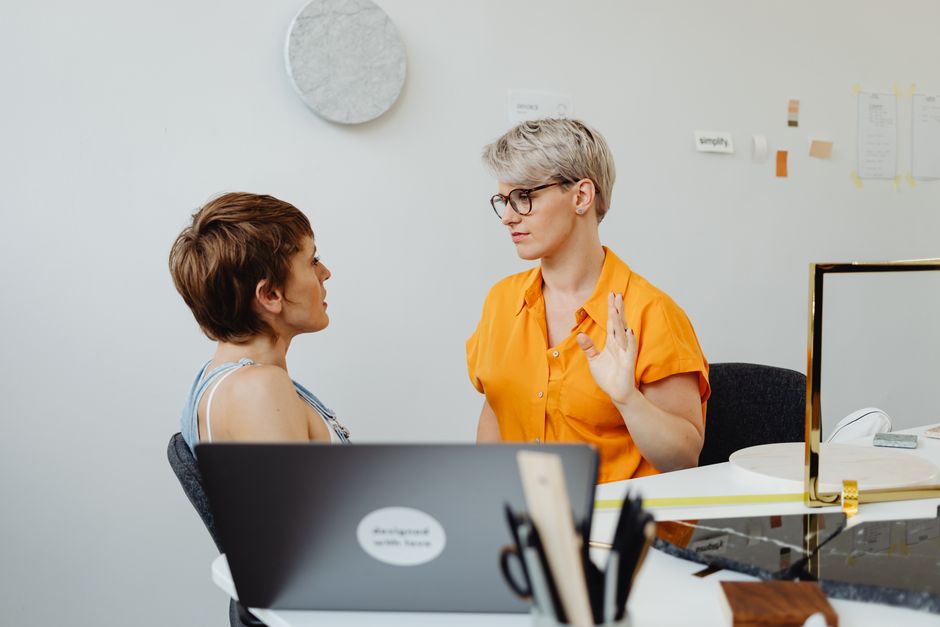 Two diverse real estate professionals sit at a minimalist desk in a bright, modern office, engaged in a collaborative discussion about a property deal.